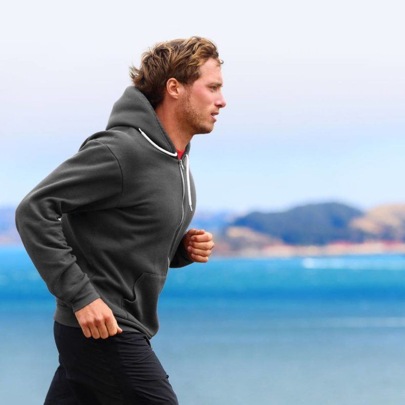 32327674 - athlete man running in sweatshirt hoodie in autumn fall by the water. male runner training outdoors jogging in nature.