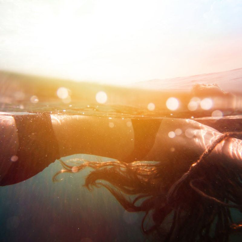 34786193 - girl underwater with sun rays and colorful sunflare