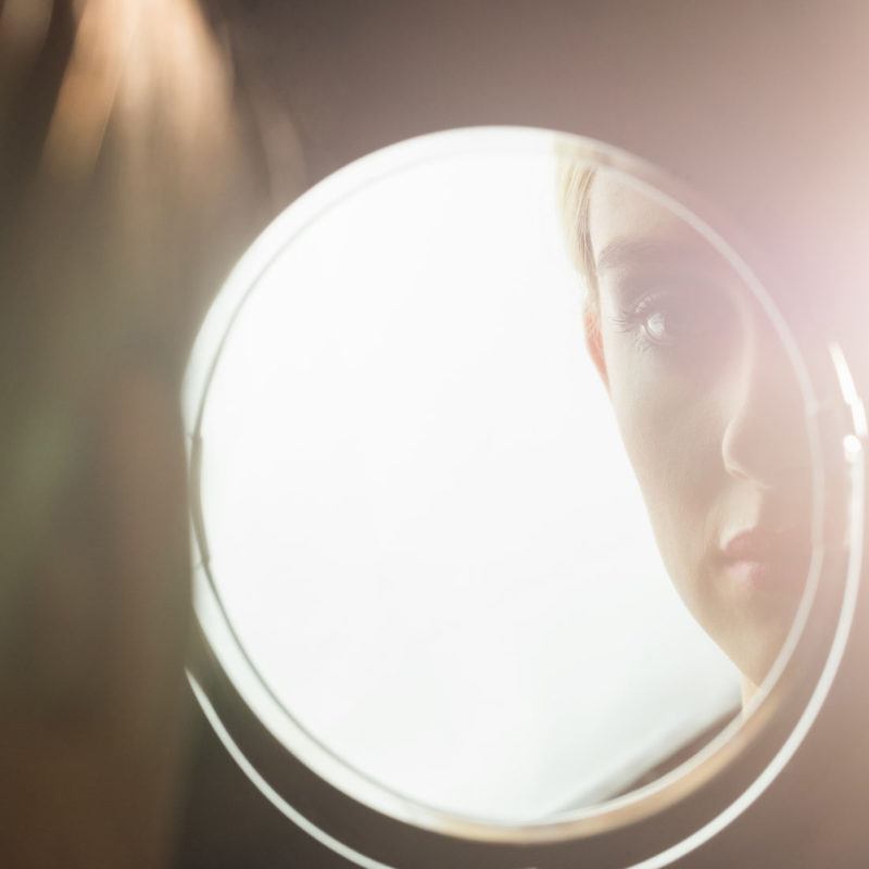 58401181 - portrait of a woman who is looking her in a mirror in a studio