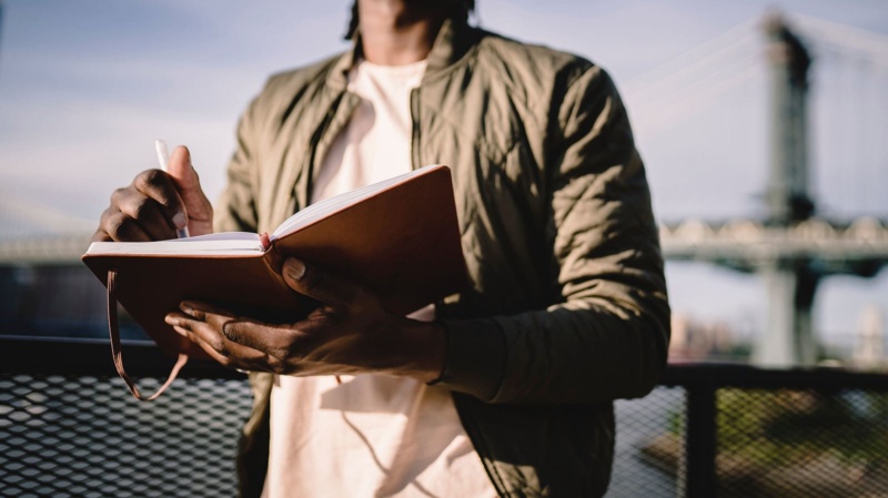 man writing manifestation journal on a bridge